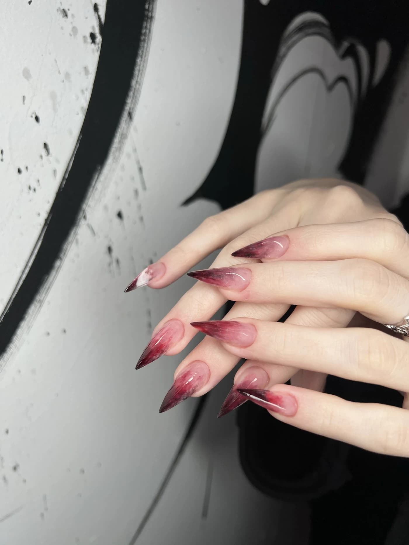 Długie paznokcie stiletto z czerwonym ombre na tle muralu — praca Martyny